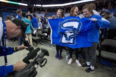 Three fans hold a Creighton flag in the student section