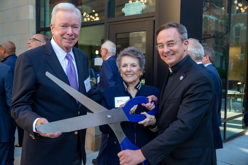 Three people pose with ceremonial, large scissors