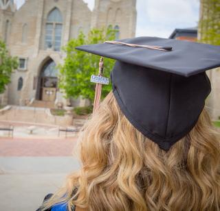 female standing before St. John's Parish Church on Creighton campus wearing a Creighton University cap and gown for graduation