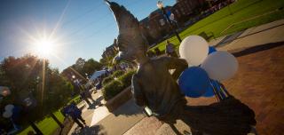 Billy Bluejay statue with blue and white balloons and Creighton campus in the background
