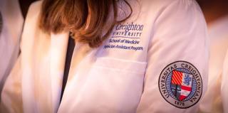 Female student wearing physician assistant white coat with Creighton seal