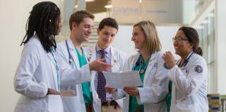 Three female and two male medical students huddle together to look at document