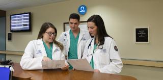 Three Creighton medical students review documents in clinic setting.