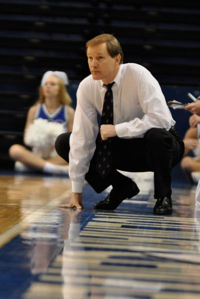 A basketball coach crouches on the sideline