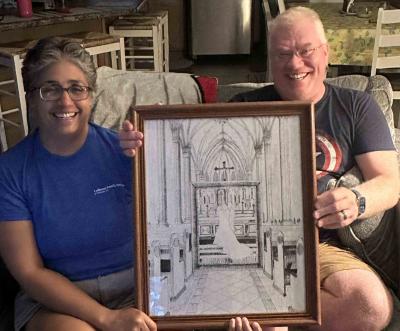 A wife and husband hold up a drawing of their wedding day