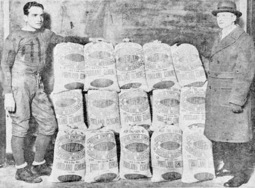 Two men stand on either side of bags of concrete