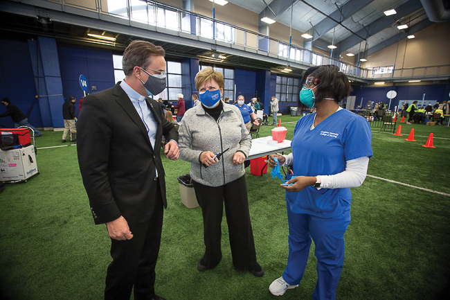 Fr. Hendrickson, and Catherine Todero, then College of Nursing dean, speak with student volunteer Anne Carter the COVID-19 Community Clinic in the Rasmussen Center in 2021.