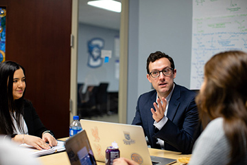 Male alumnus speaks to two female students in a meeting room.