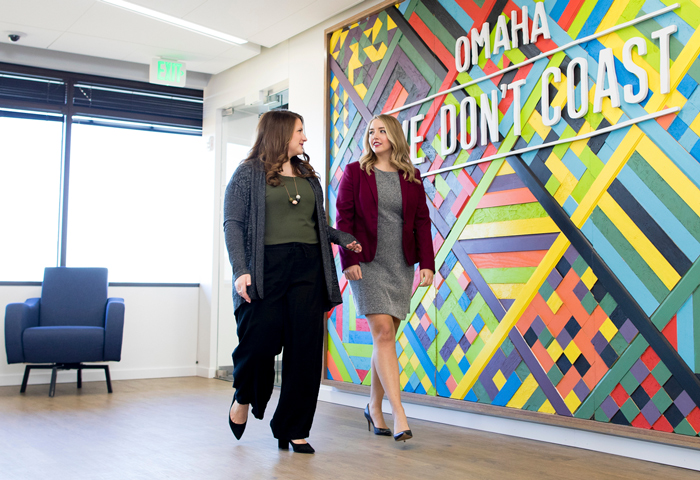 two women walking in front of sign that reads Omaha We Don't Coast