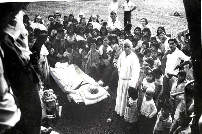 The Cururu's Father Marquard Paterek, wearing a white robe, supervises the loading of an injured passenger onto a rescue plane.