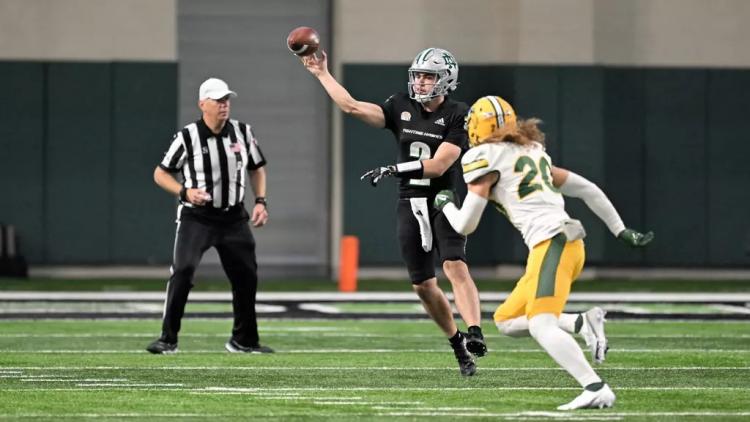 A photo of college football action with a referee in the background