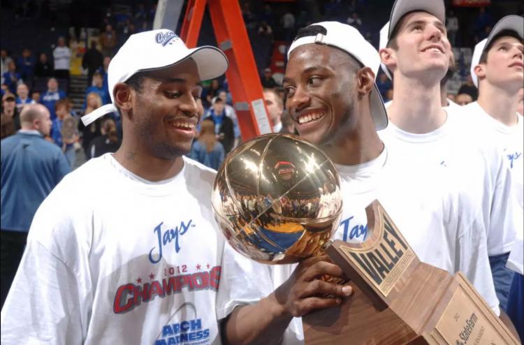 One basketball player holds a trophy as he smiles at a teammate