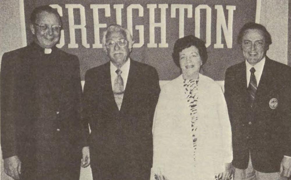 A photo of four people in front of a Creighton sign