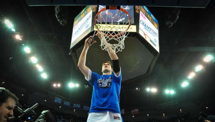 A player uses scissors to cut down the net on a basketball hoop