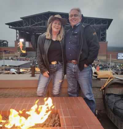 A couple smiles in front of a fire