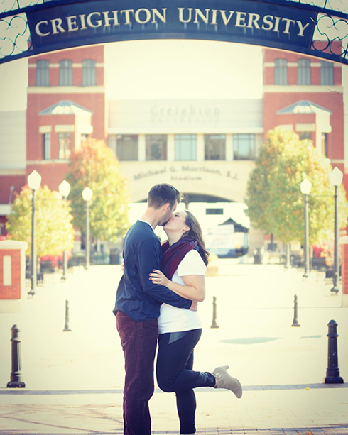Amanda Reinhart and Jack Pritchard kiss in front of the Creighton sign.