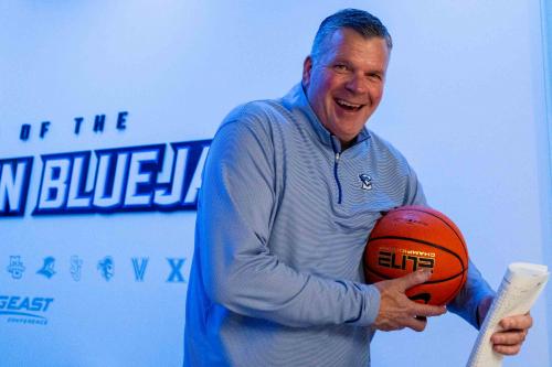 A smiling coach carries a basketball as he enters the locker room