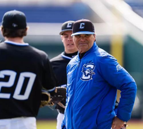 A baseball coach stands on the field next to a couple players