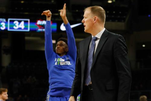 A player shoots a basketball in front of a coach