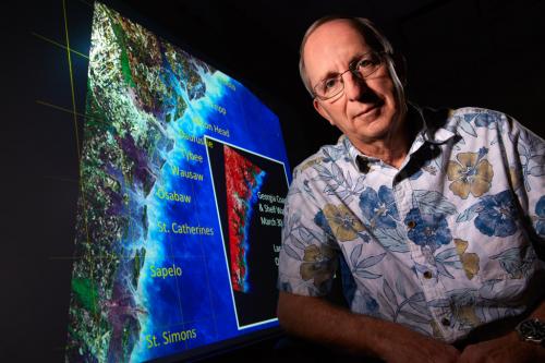 A man poses for a photo while sitting next to a map of the Georgia coast.