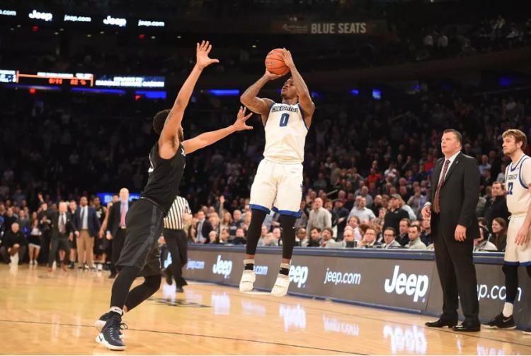 A player shoots a jump shot as a defender reaches to contest