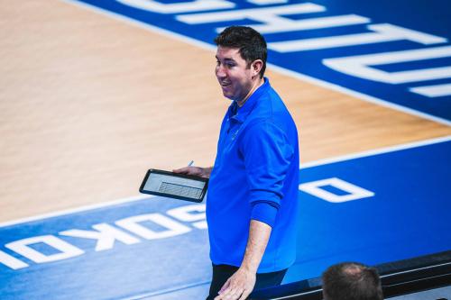A volleyball coach stands on the sideline
