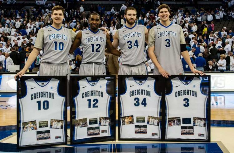 Four basketball players stand together in front of their framed jerseys