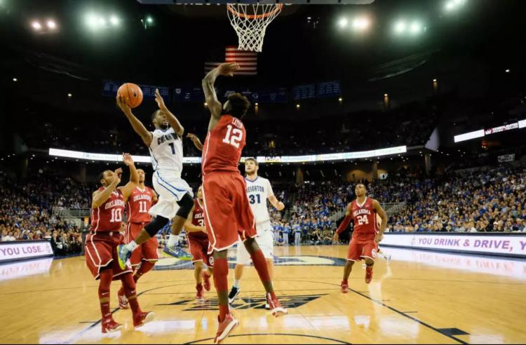 A basketball player attempts a shot over a leaping defender