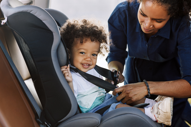 Mother buckles child into car seat.