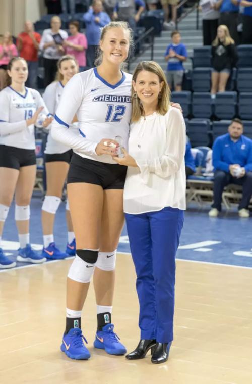 A volleyball player and her coach stand together and smile