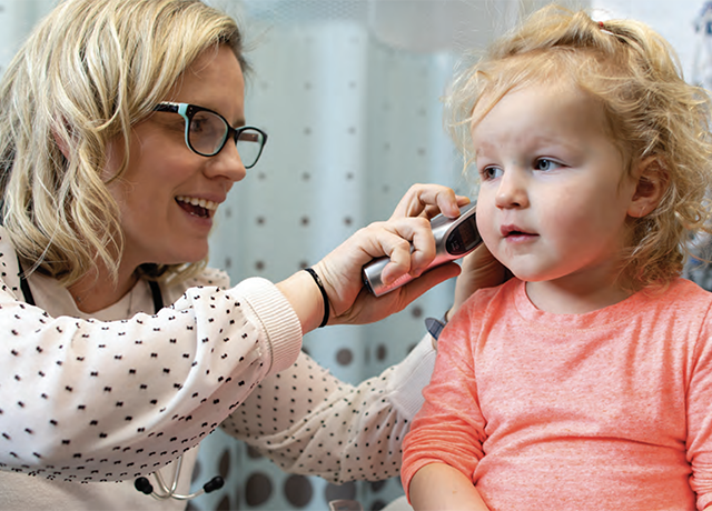 A nurse looks into a child's ear during a checkup.