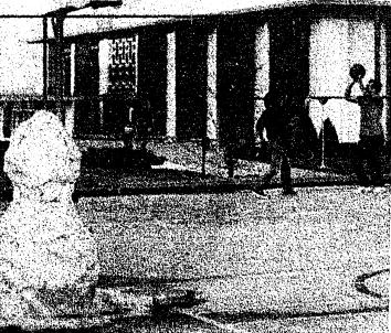 A black and white photo of a snowman with two people playing basketball in the background