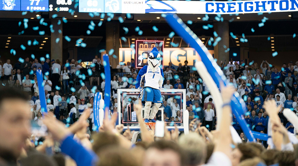 Billy Bluejay stands on top of the basketball hoop as the fans celebrate