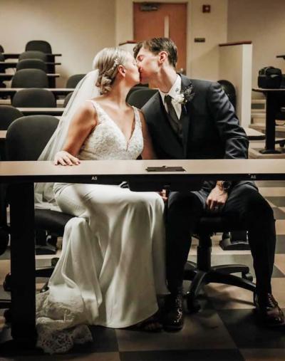 A woman in a wedding dress kisses her husband in a classroom