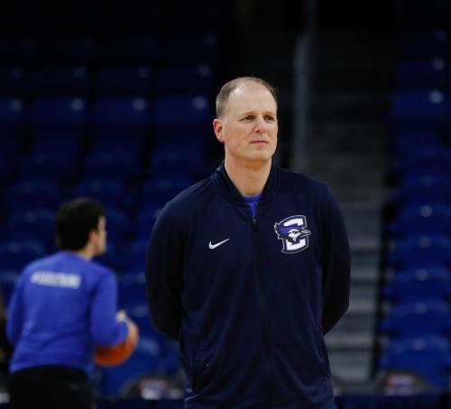 A basketball coach stands with his arms behind his back