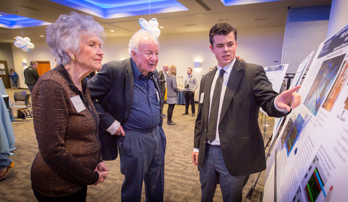 A Ferlic fellow presents a poster of his research to Teresa Kolars Ferlic and Randolph Ferlic, BS’58, MD’61.