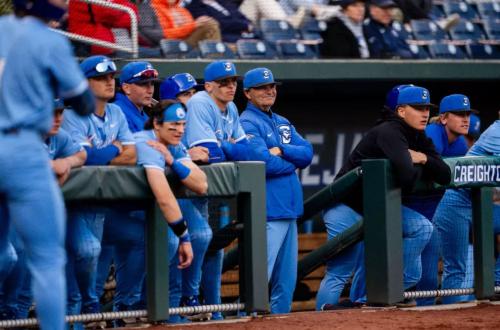 A baseball coach stands with his team inside the dugout