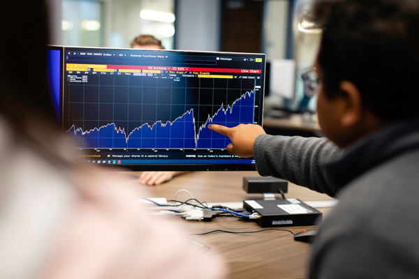 A student pointing a stocks graph on a screen.