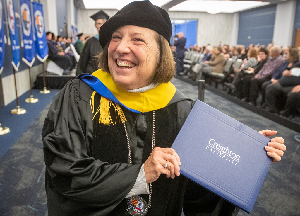 A woman smiles as she holds a Creighton degree