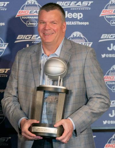 A coach smiles as he holds a trophy