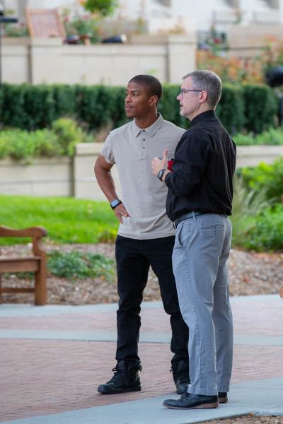 Two men talk together on a sidewalk