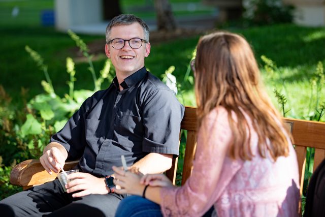 Father Jeff Sullivan, SJ, speaks with a student at a bench on the Mall.