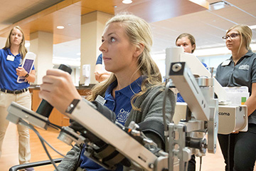 An OT student demonstrates assistive tech while her class watches.