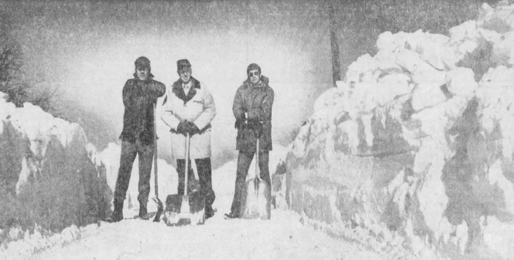 Three men stand next to huge snow piles