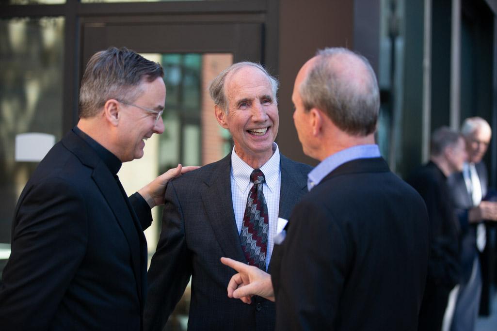 Three men talk before a ribbon cutting event