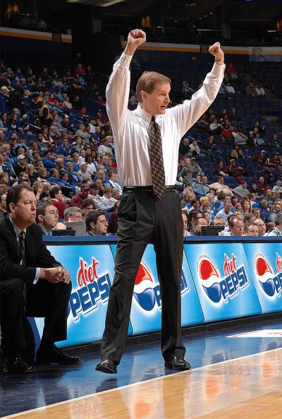 A basketball coach raises both arms on the sideline