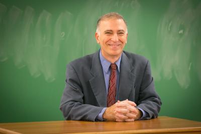 A professor smiles in front of chalkboard
