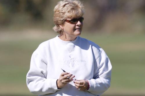 A women's golf coach stands on the course