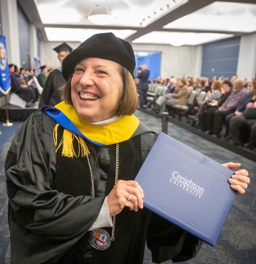 A woman smiles as she holds a Creighton degree