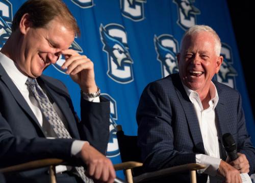 Two men laughing while speaking on a panel